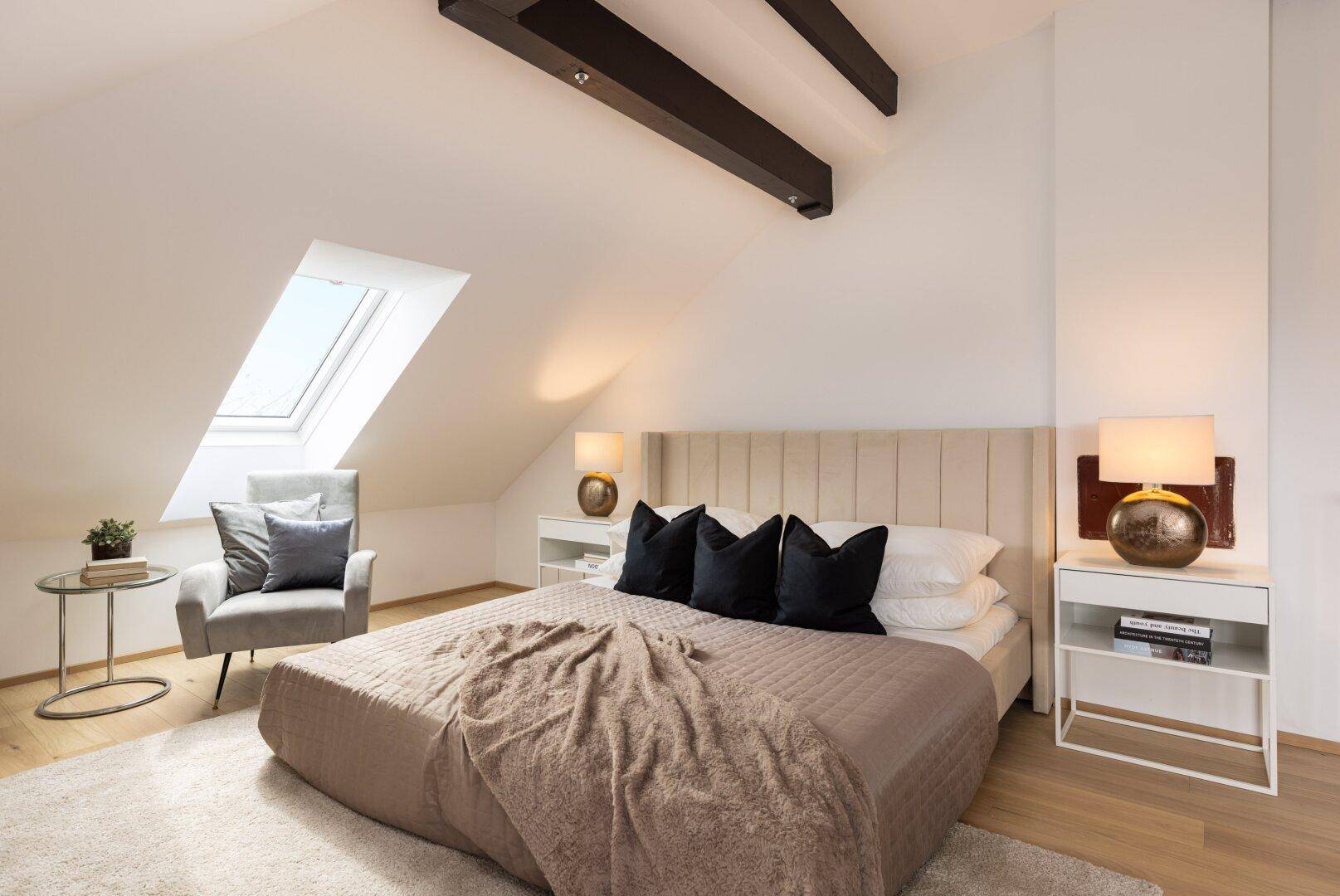 Schlafzimmer im Dachgeschoss mit Holzbalken, Bett und Dachfenster.