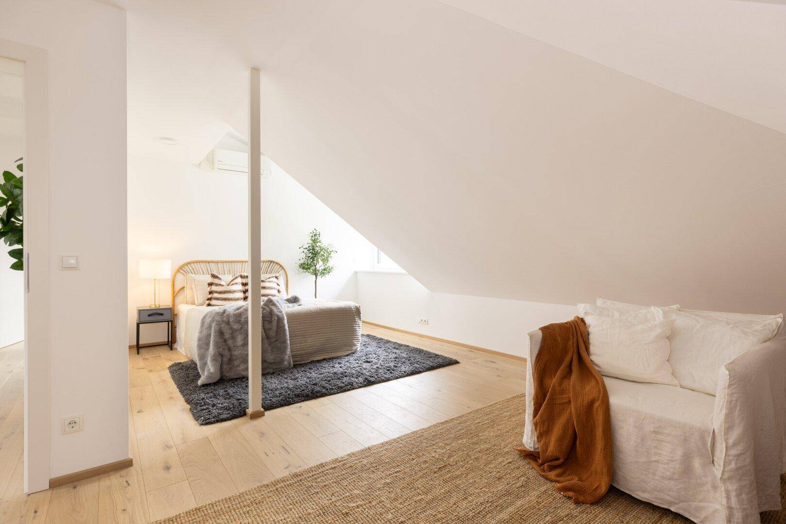 Helles Schlafzimmer im Dachgeschoss mit Bett, Lesesessel und schrägen Wänden.