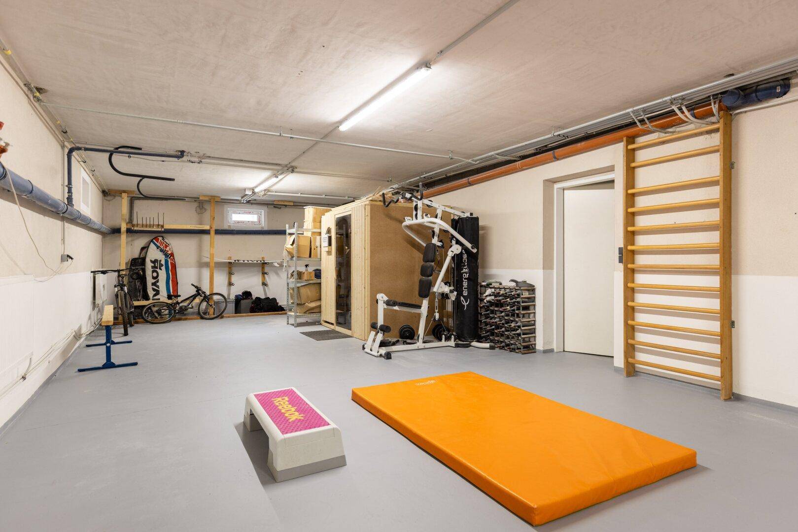 Geräumiger Fitnessraum im Keller mit verschiedenen Trainingsgeräten und Sauna.