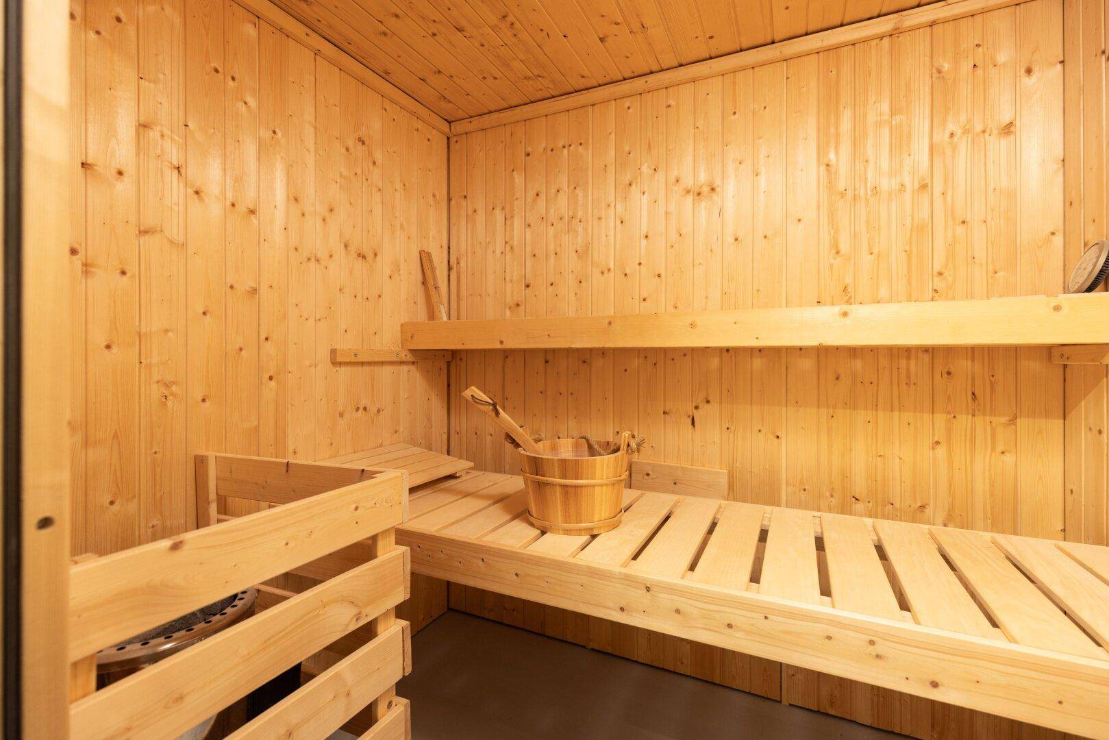 Innenansicht einer traditionellen Holzsauna mit Bänken und Eimer.