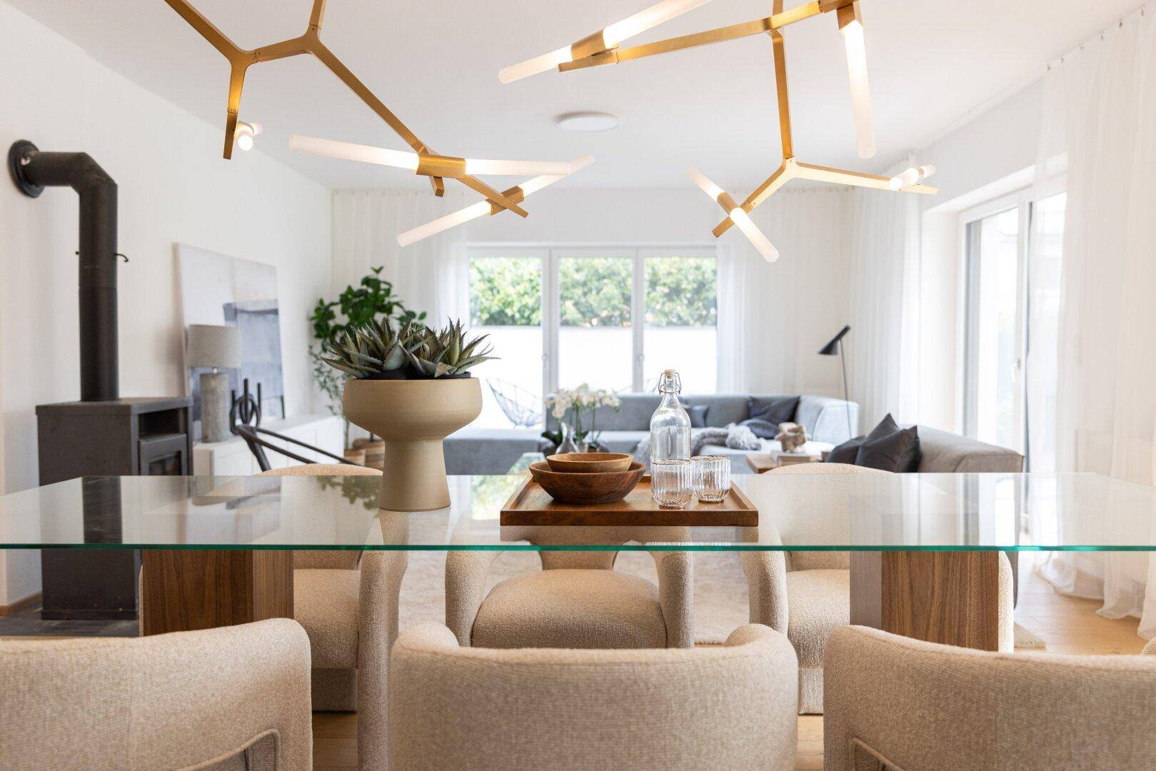 Blick vom Essbereich in das Wohnzimmer mit modernem Glastisch und Designerleuchten.