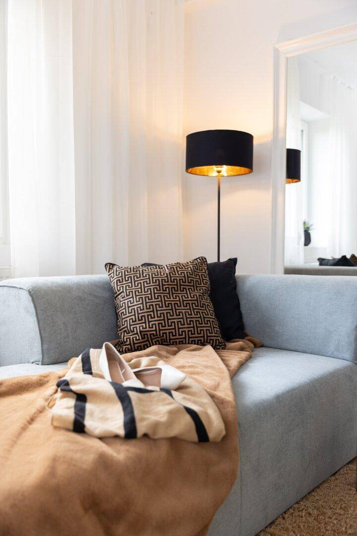 Gemütliche Chaiselongue mit Decke und Kissen neben einer Stehlampe.