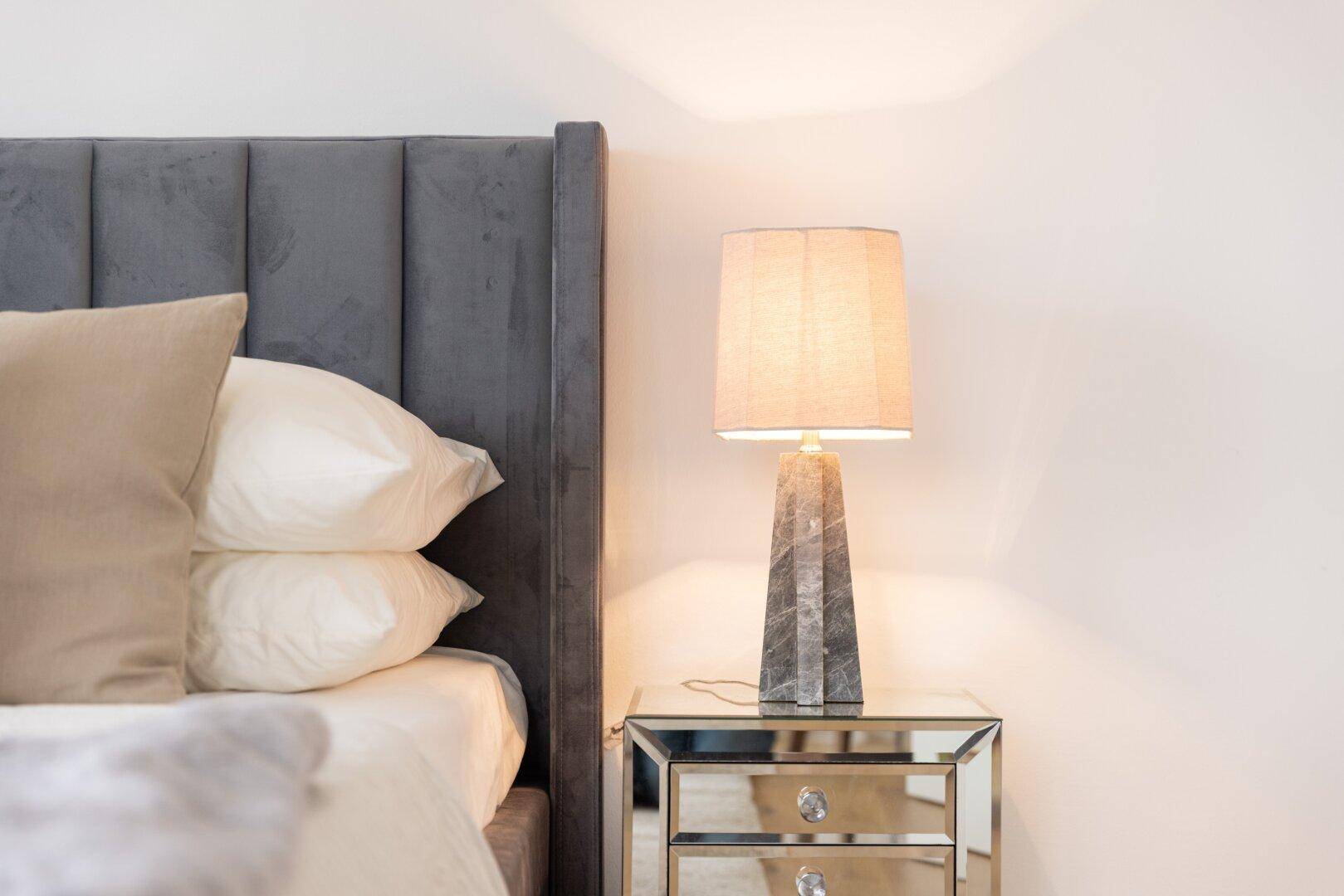 Detailansicht eines Nachttisches mit Lampe und Kissen auf dem Bett.