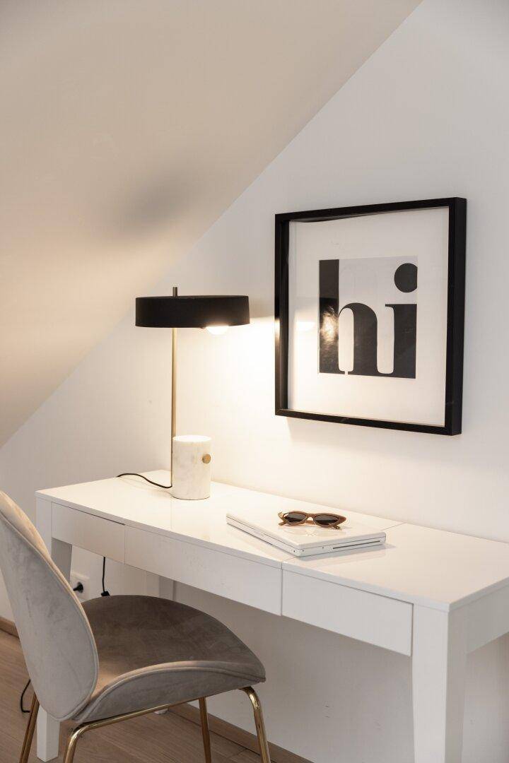 Schreibtisch mit Lampe und gerahmtem Bild in einem hellen Dachzimmer.