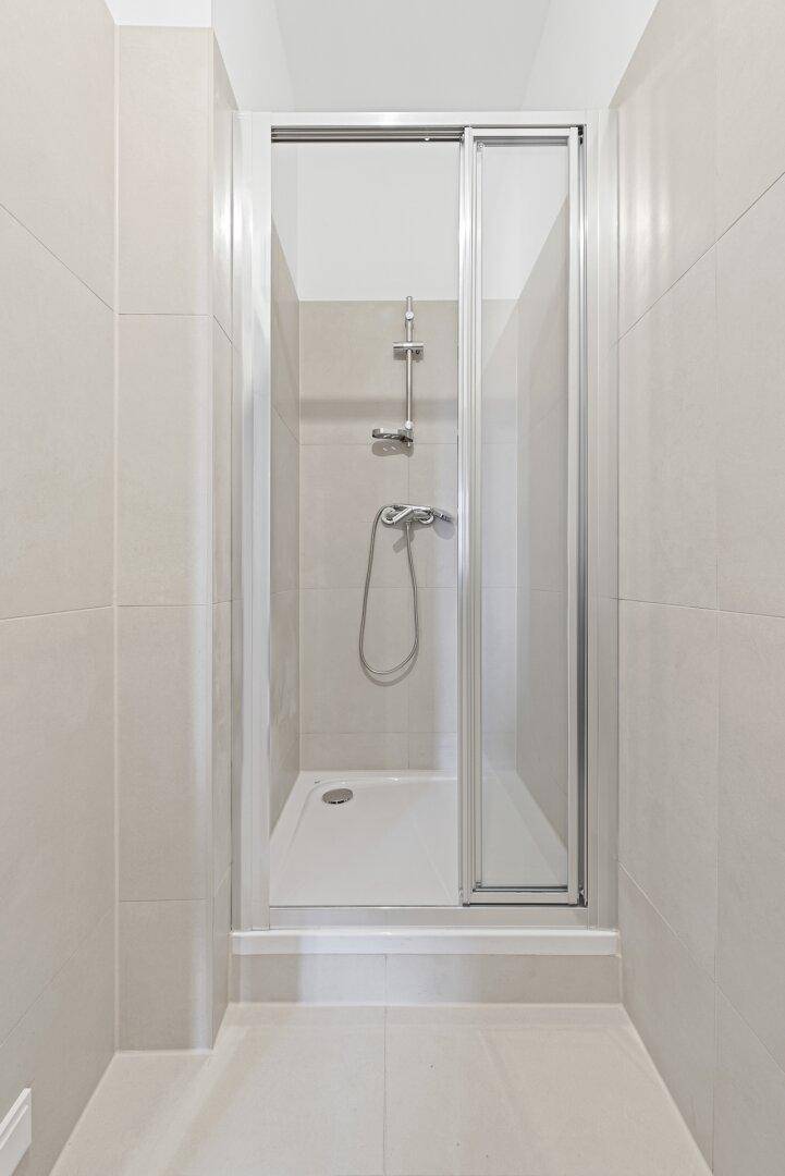 Modernes Badezimmer mit Duschkabine und hellen Fliesen an Wänden und Boden.