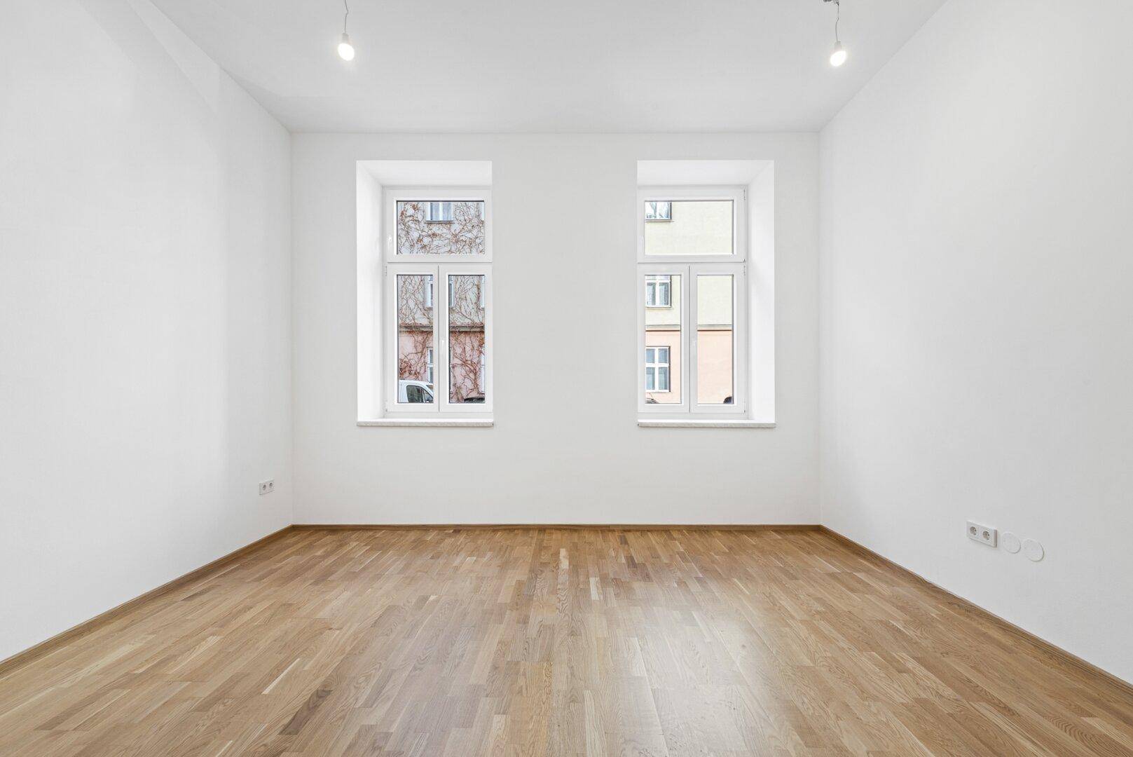 Unmöblierter Raum mit Holzboden und zwei Fenstern, bietet viel natürliches Licht.