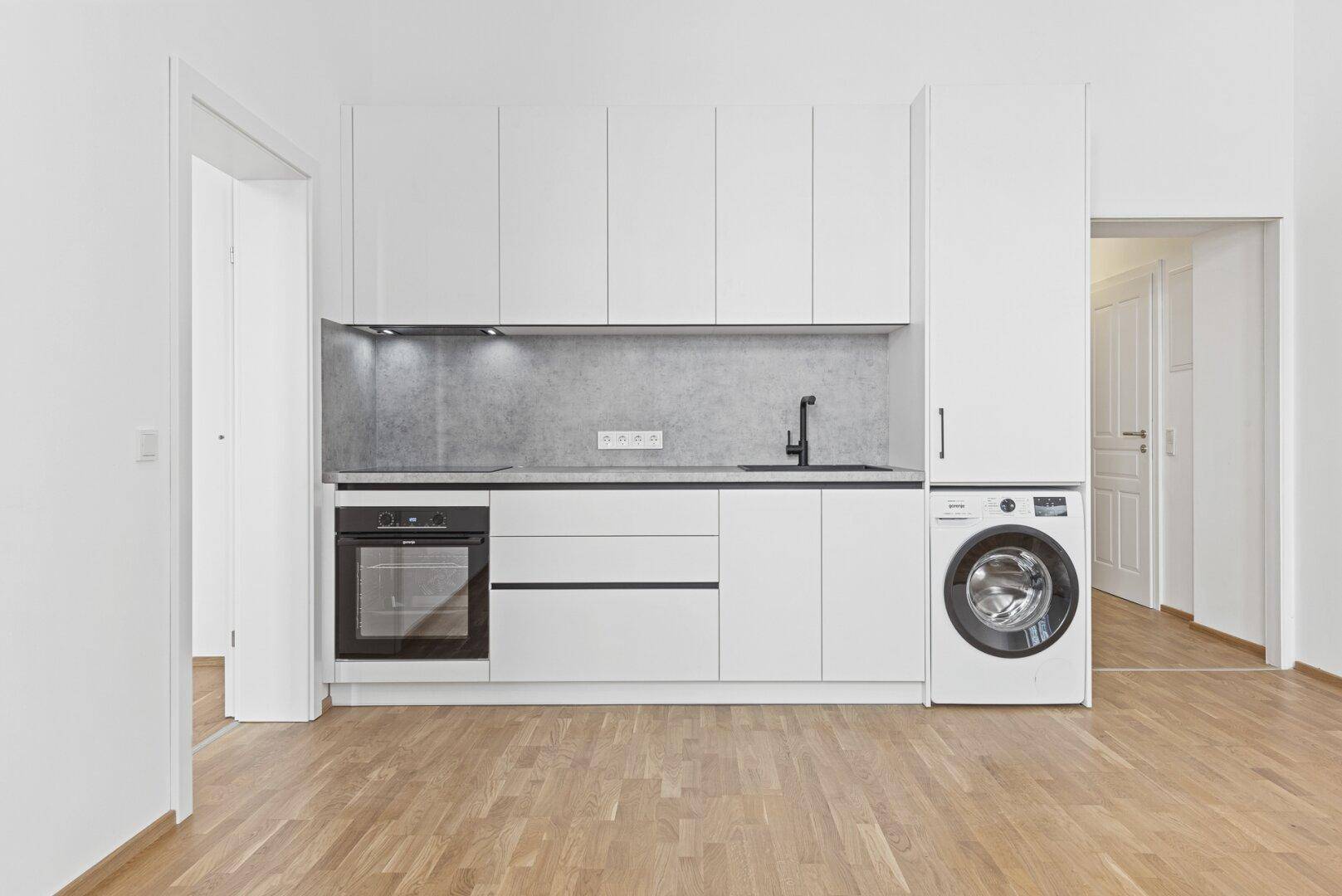 Kompakte Küchenzeile mit modernen weißen Schränken, Backofen und integrierter Waschmaschine.
