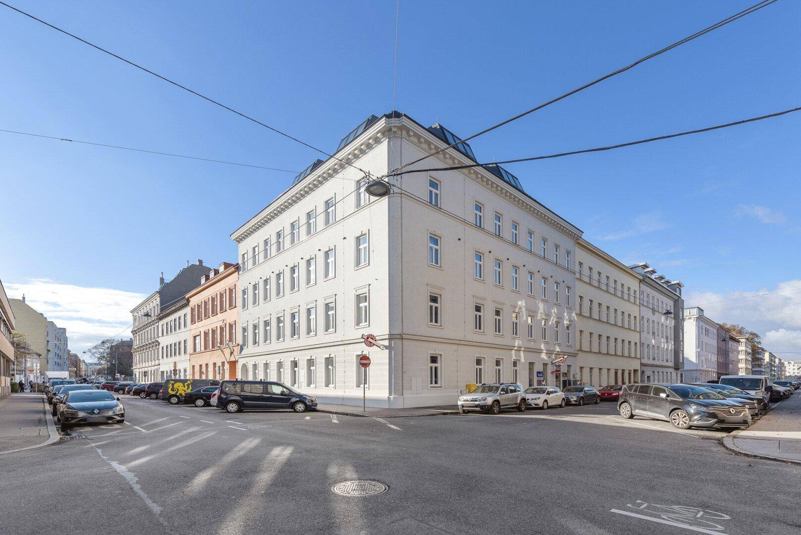 Eckgebäude mit klassischer Architektur und vielen Fenstern an einer städtischen Straße.