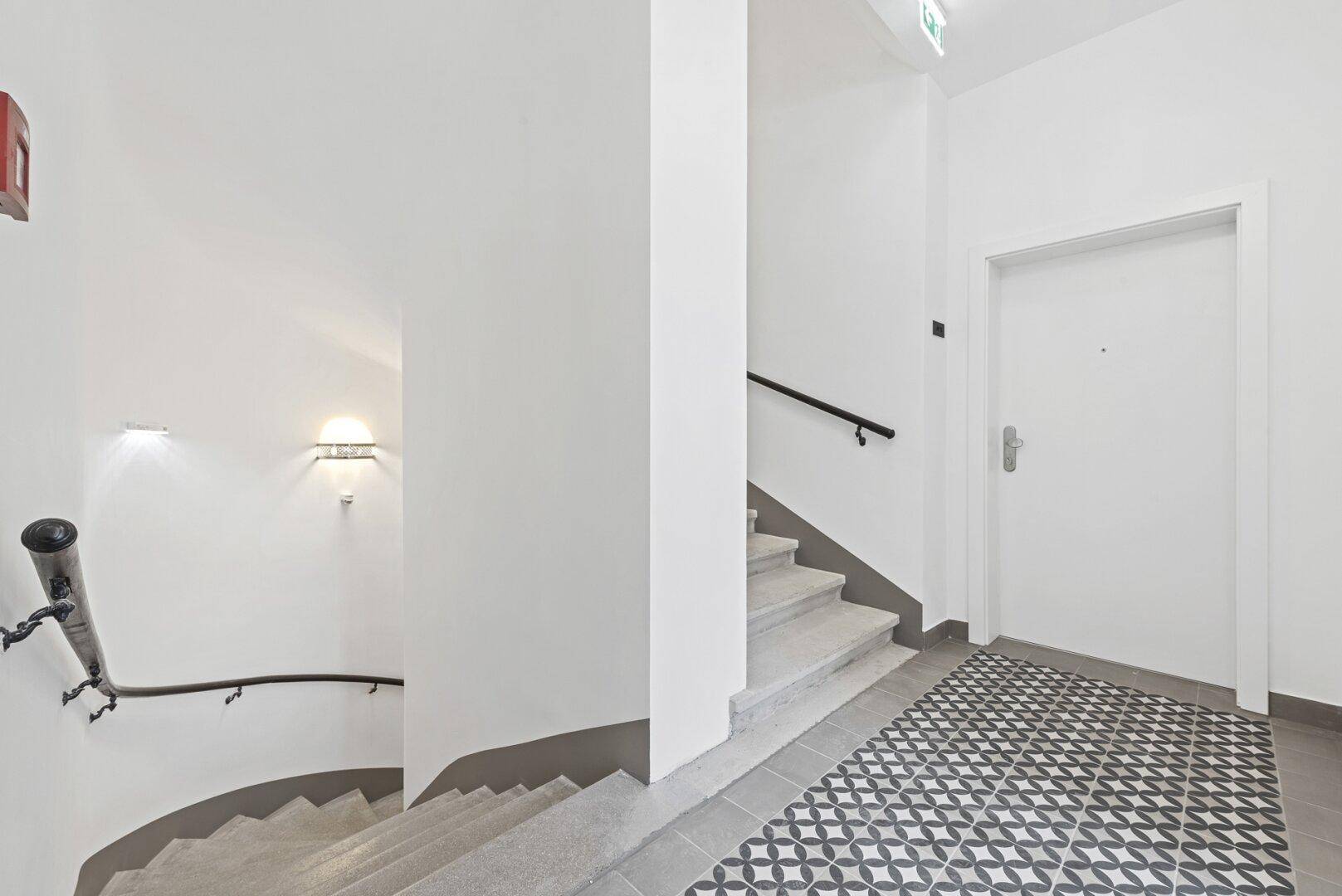 Treppenhaus mit Steinstufen und dekorativem Fliesenboden im Eingangsbereich des Gebäudes.