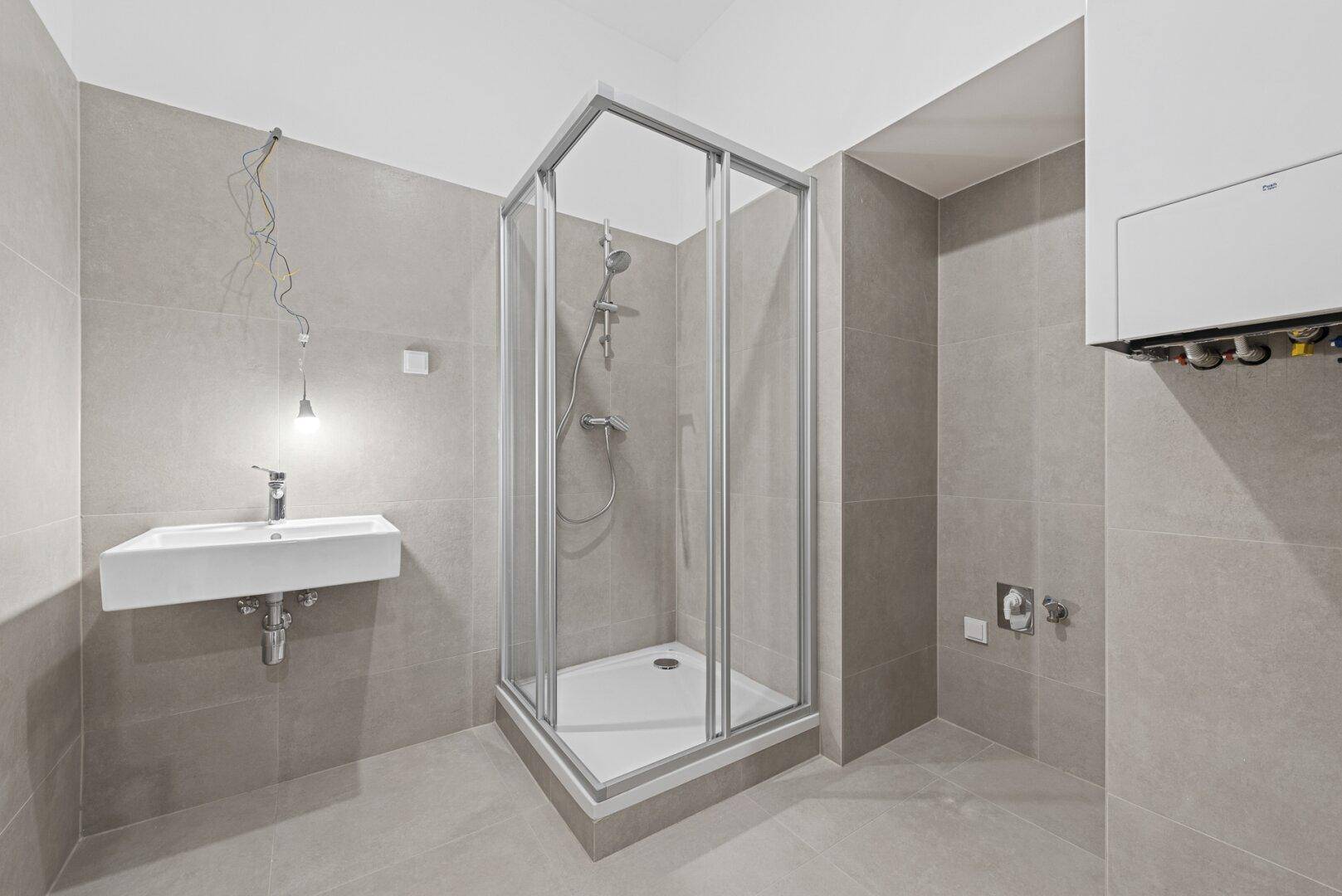 Modernes Badezimmer mit Duschkabine, Waschbecken und grauen Wand- und Bodenfliesen.