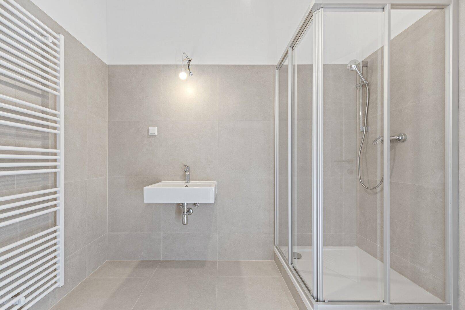 Modernes Badezimmer mit grauen Fliesen, Duschkabine und beheiztem Handtuchhalter.