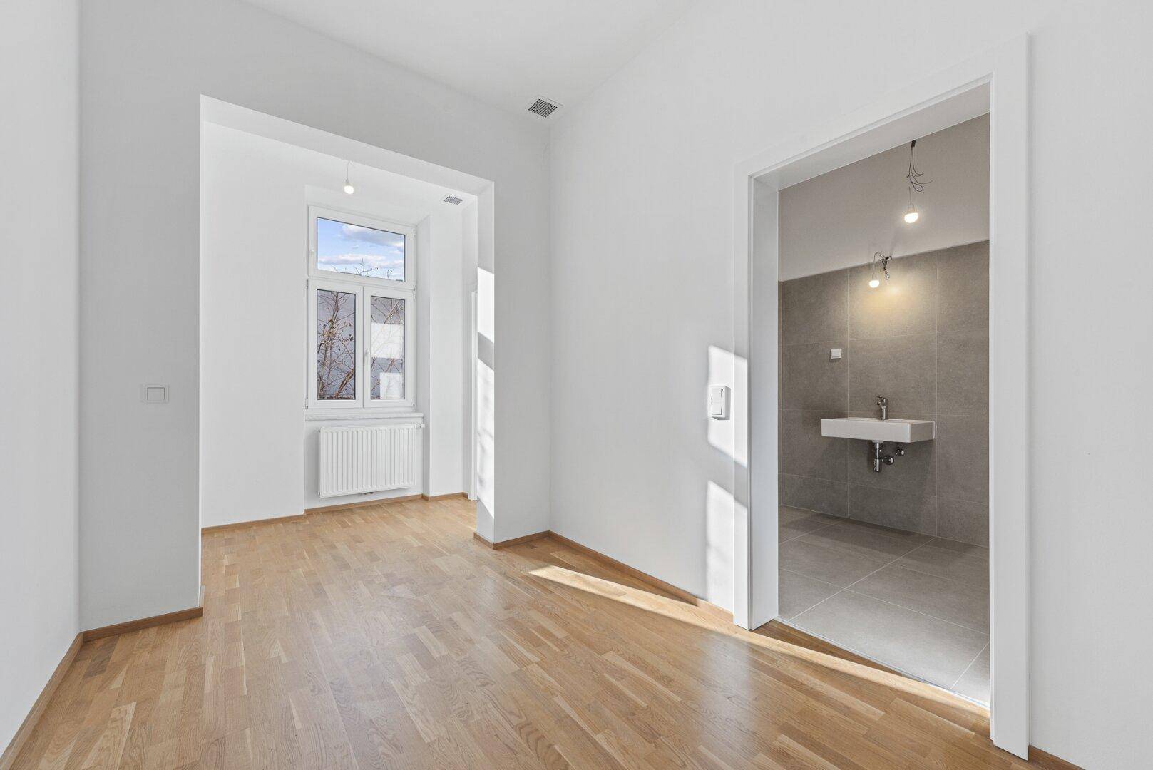 Heller Raum mit Parkettboden und Zugang zu einem modernen Badezimmer.
