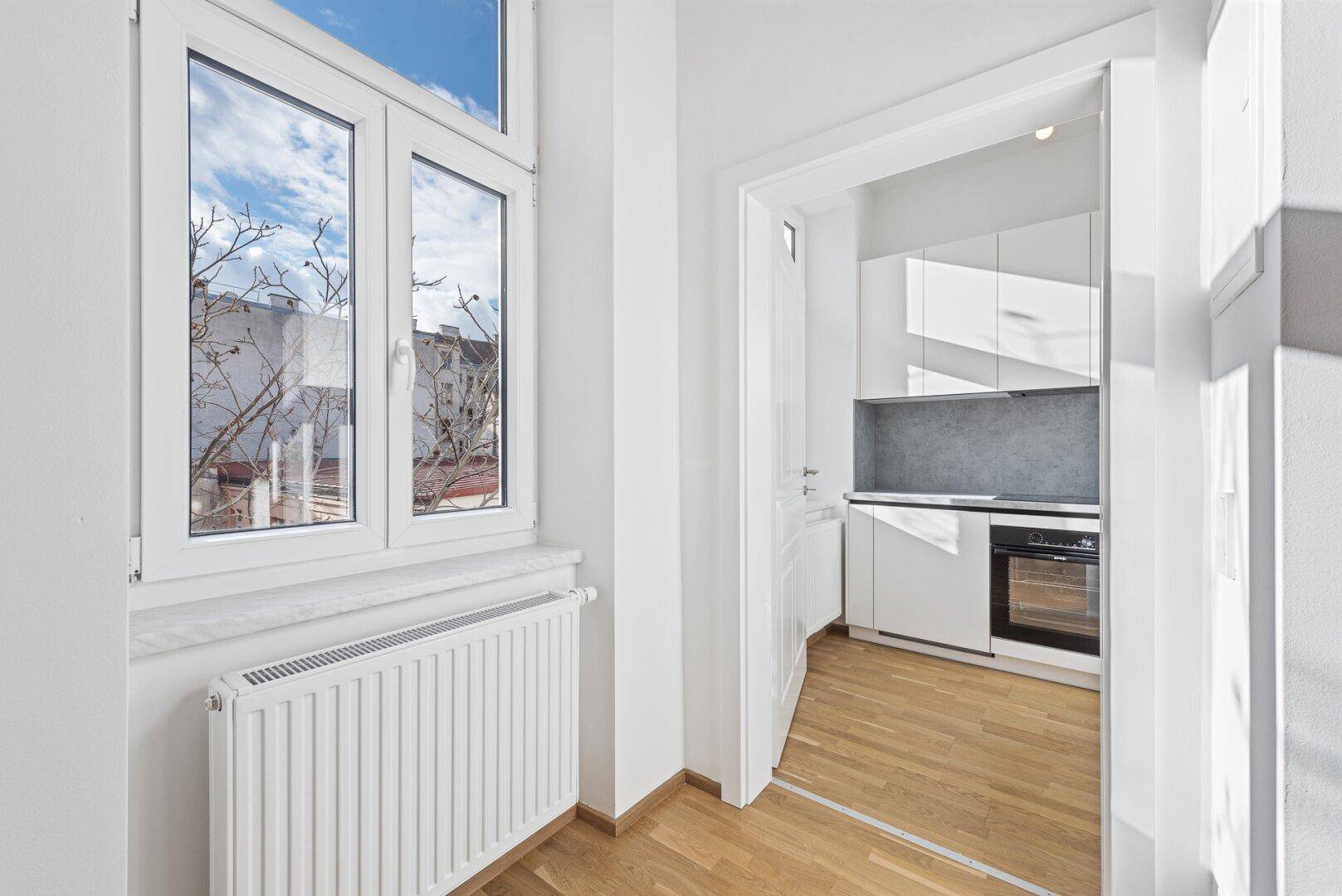 Heller Raum mit Fenster und Blick auf eine moderne, weiße Einbauküche.