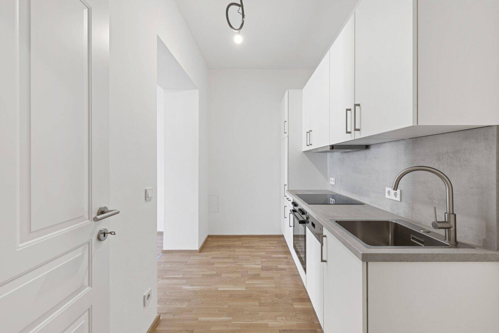 Moderne Küchenzeile mit weißen Schränken, Spüle und Kochfeld, daneben ein Holzboden.