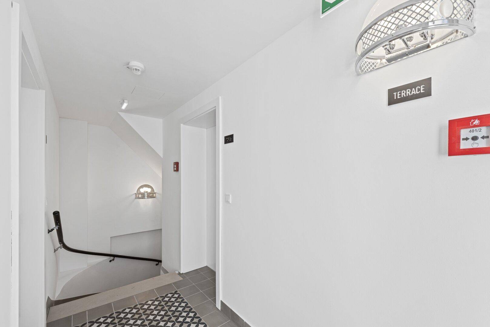 Heller Treppenabsatz mit modernem Fliesenboden und Hinweisschild zur Terrasse, gut beleuchtet.