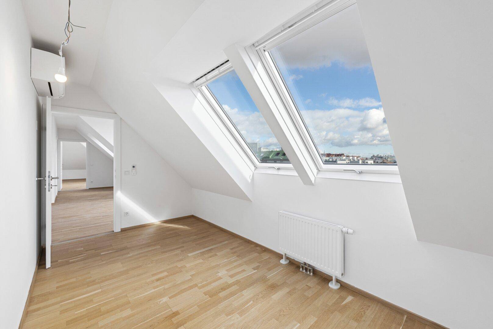 Helles Dachzimmer mit schrägen Fenstern, Holzboden und Klimaanlage, bietet viel natürliches Licht.