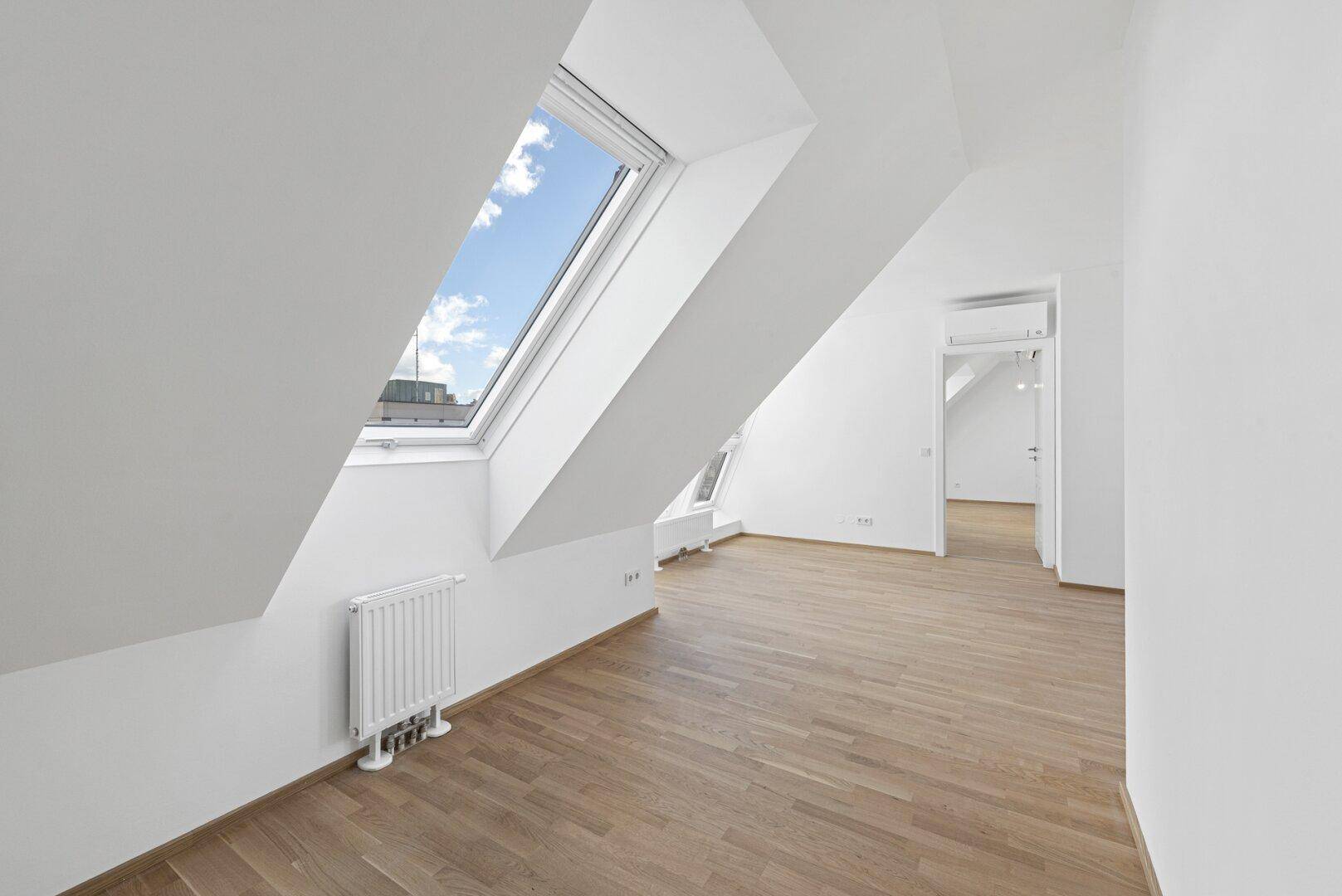 Helles Dachzimmer mit schrägem Fenster, Holzboden und viel Tageslicht, ideal als Schlaf- oder Arbeitszimmer.