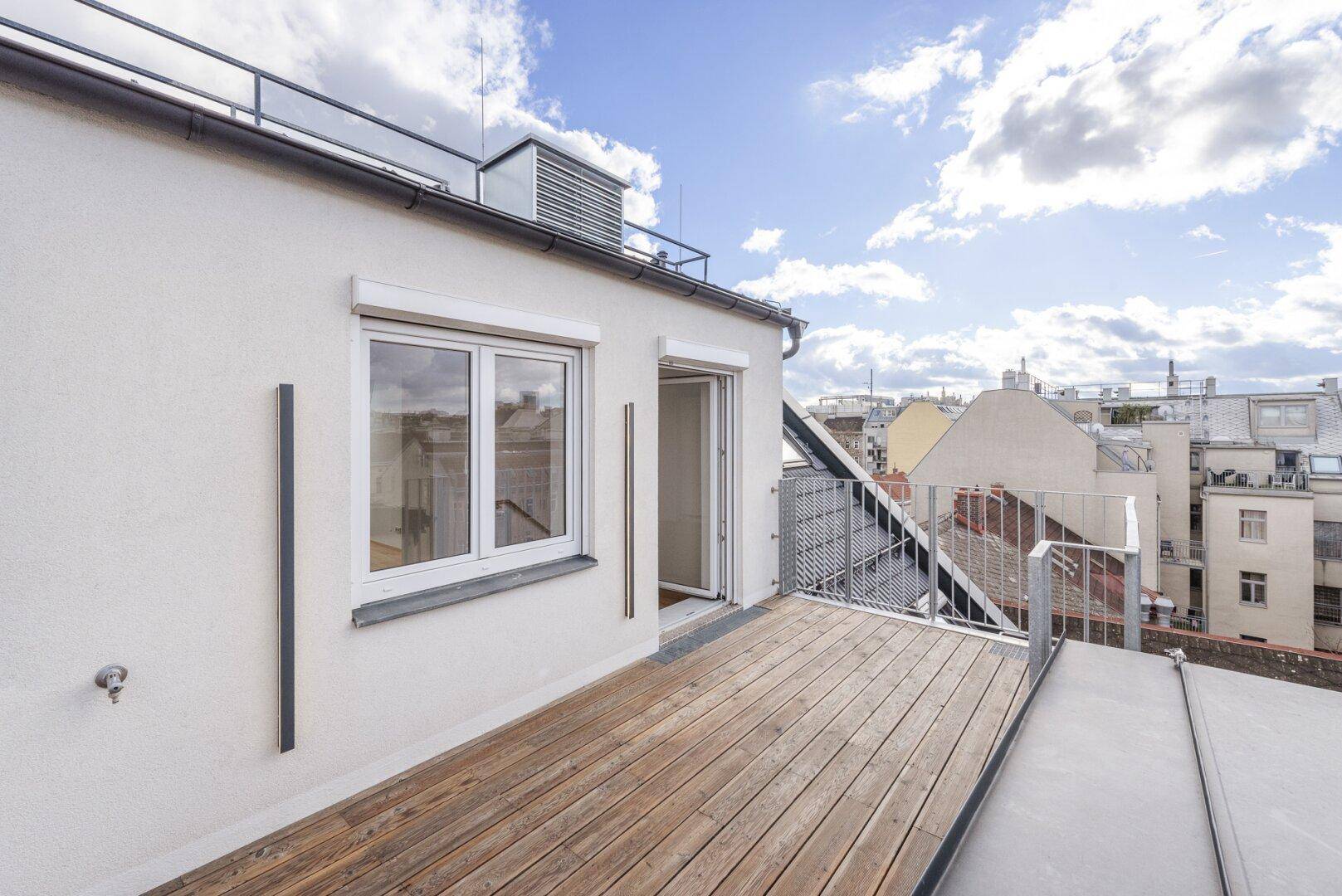 Geräumige Dachterrasse mit Holzbelag und Metallgeländer, ideal für Entspannung im Freien mit Stadtblick.