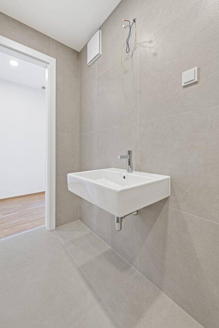 Modernes Badezimmer mit grauen Fliesen und einem einzelnen Waschbecken, bereit zur Fertigstellung.