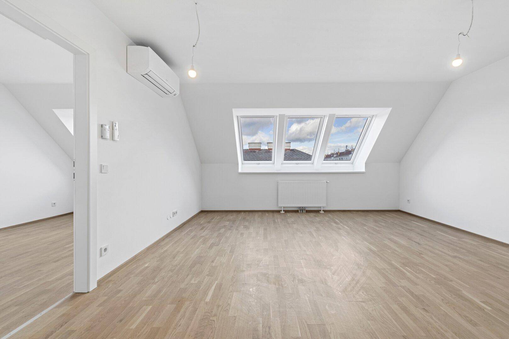 Geräumiger Dachgeschossraum mit Holzparkett, Dachfenstern und Klimaanlage, ideal als Wohnzimmer.