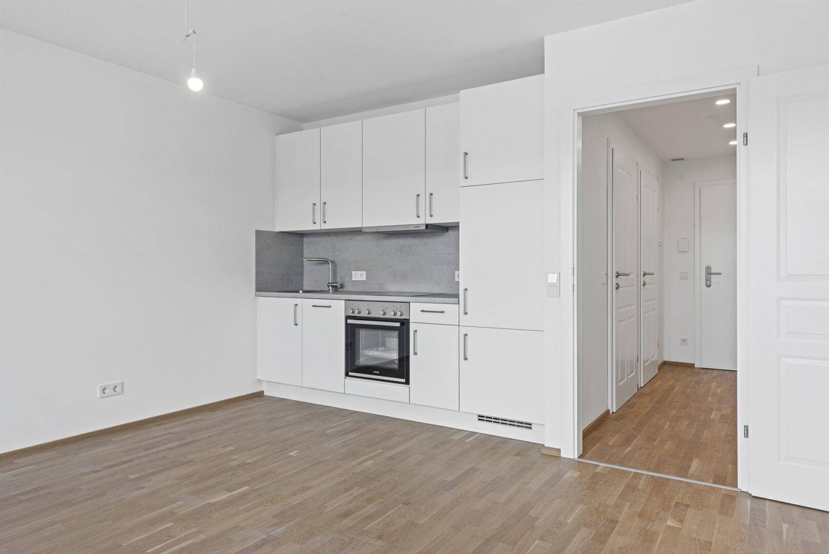 Moderne Küchenzeile mit weißen Schränken, integriertem Backofen und Spüle in hellem Raum.