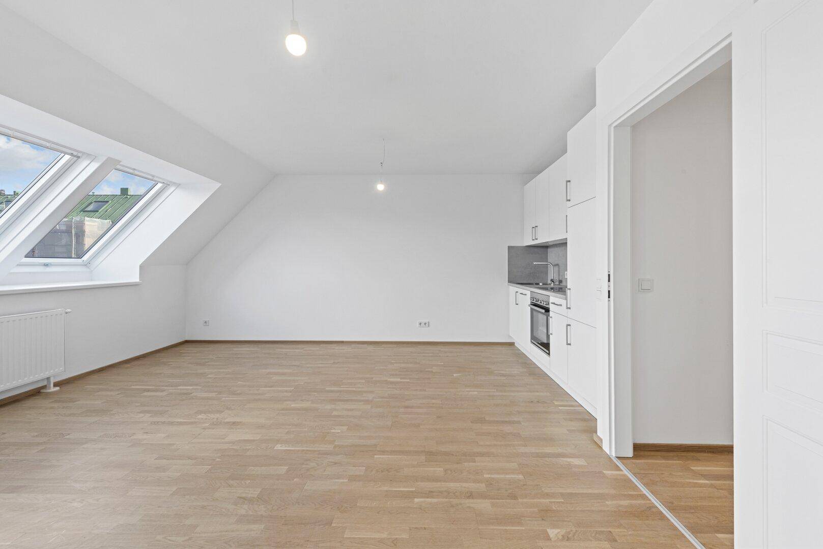Heller offener Wohnbereich mit integrierter Küchenzeile, Holzparkett und Dachfenstern.