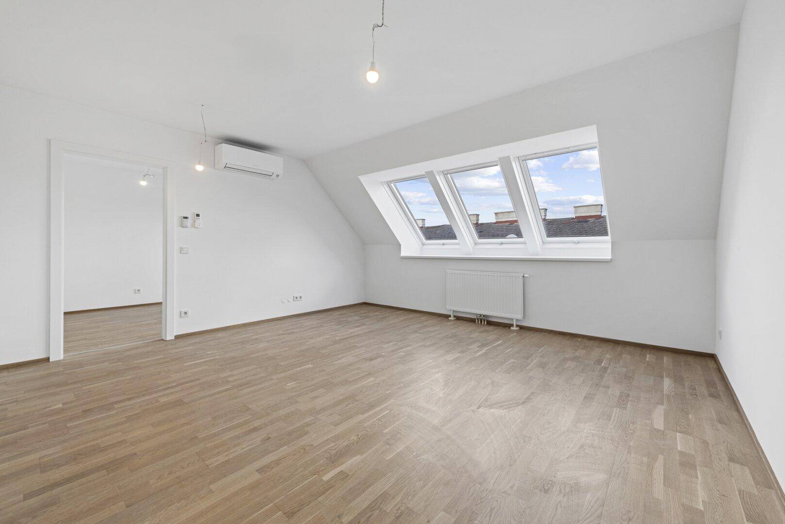 Heller Dachgeschossraum mit Holzparkett, drei Dachfenstern und Klimaanlage, ideal für Wohnzwecke.