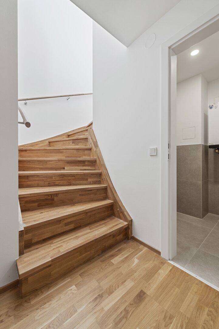 Helle Holztreppe mit Metallgeländer, die in die obere Etage führt, mit angrenzendem Badezimmer.