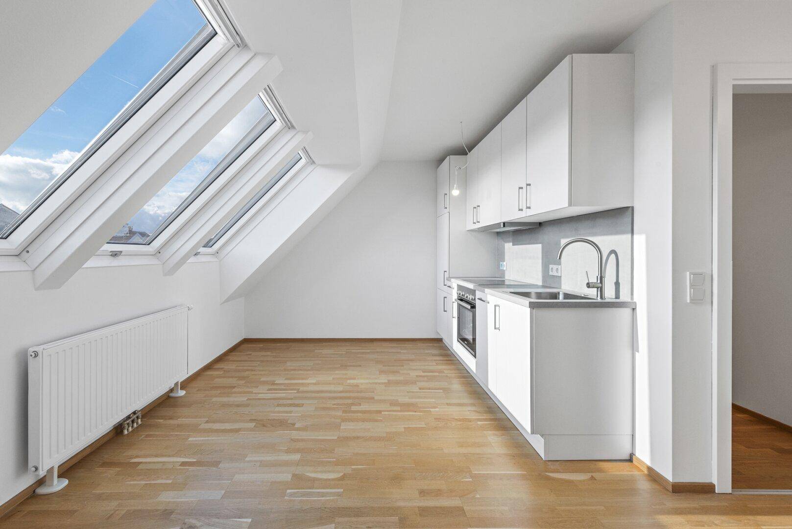 Moderne Küchenzeile in einer Dachgeschosswohnung mit Holzboden und großen Dachfenstern.