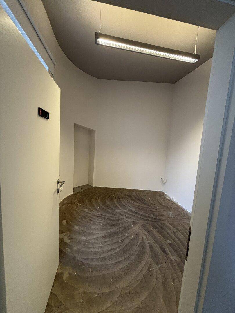 Kleiner, heller Raum mit einzigartigem Betonbodenmuster und moderner Deckenbeleuchtung, vielseitig nutzbar.