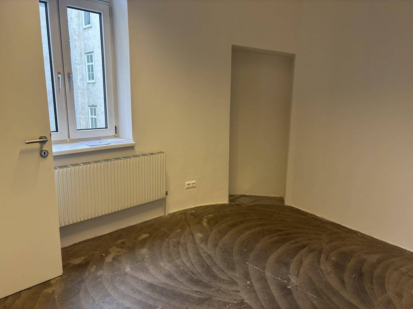 Heller, kleiner Büroraum mit Fenster und Heizkörper, bietet eine ruhige Arbeitsumgebung.
