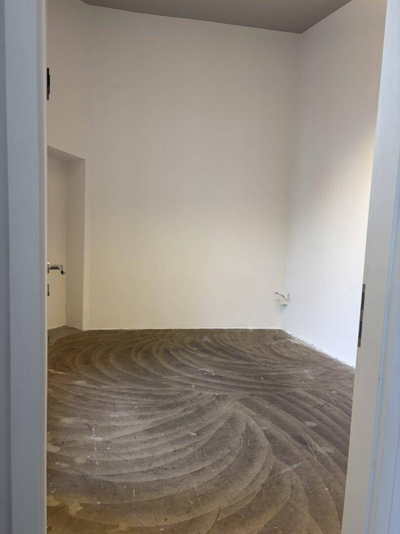 Leerer Raum mit markantem Betonbodenmuster und schlichten weißen Wänden, ideal für ein kleines Büro.