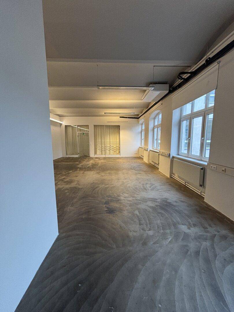 Heller, leerer Büroraum mit großen Fenstern und Betonboden, bereit für individuelle Gestaltung und Nutzung.