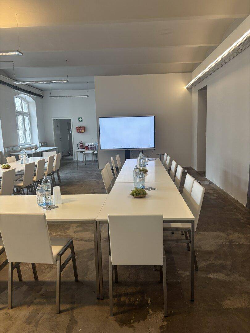 Moderner Konferenzraum mit großem Bildschirm und U-förmiger Tischordnung, ideal für Präsentationen und Meetings.