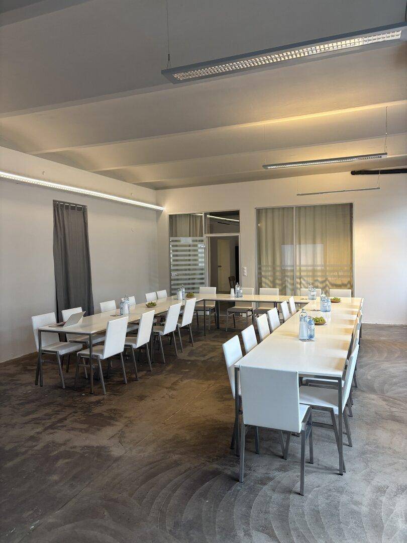 Geräumiger Konferenzraum mit mehreren Tischreihen und Stühlen, bereit für größere Veranstaltungen oder Schulungen.