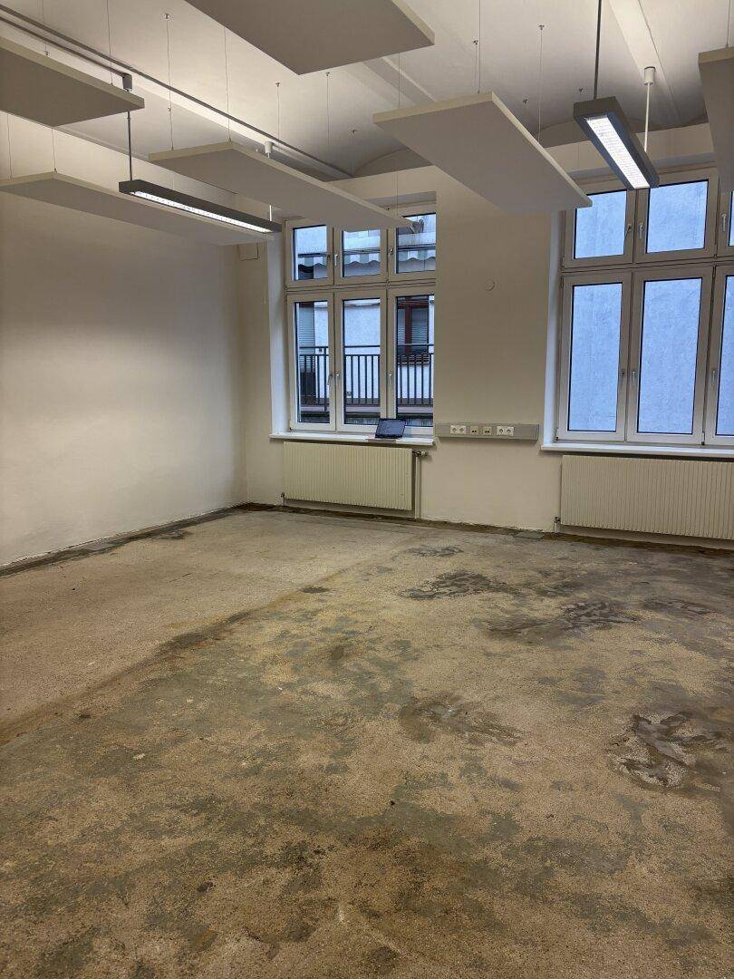 Geräumiger Büroraum mit großen Fenstern, Betonboden und schallabsorbierenden Deckenplatten für eine angenehme Akustik.