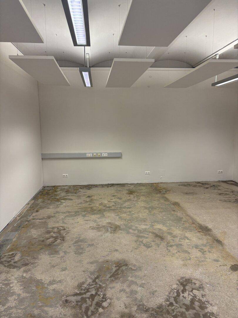 Leerer Büroraum mit Betonboden, schallabsorbierenden Deckenplatten und praktischer Wandsteckdosenleiste.