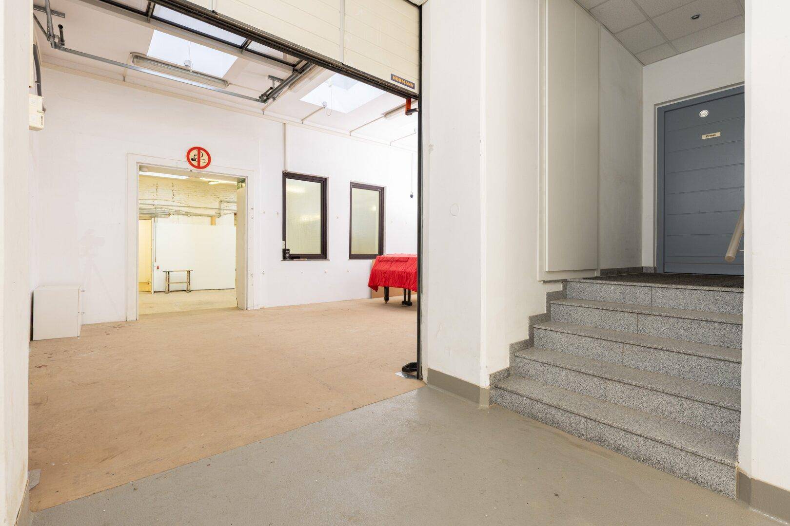 Eingangsbereich zu einem großen Lagerraum mit Treppe und einer grauen Tür.