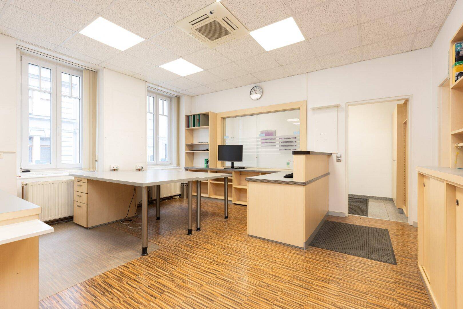 Helles Büro mit großen Fenstern, Holzoptikboden und Empfangsbereich, gut ausgestattet.