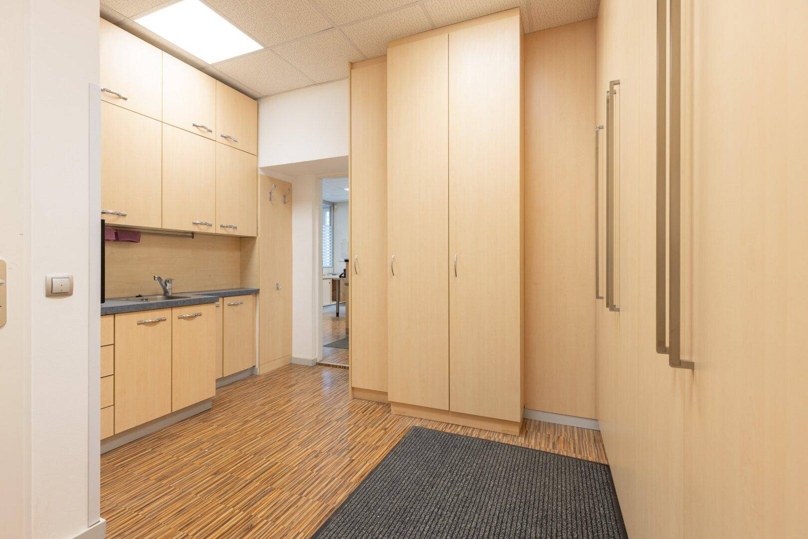 Kleiner Küchenbereich mit Holzschränken und Spüle, ideal für eine Teeküche im Büro.