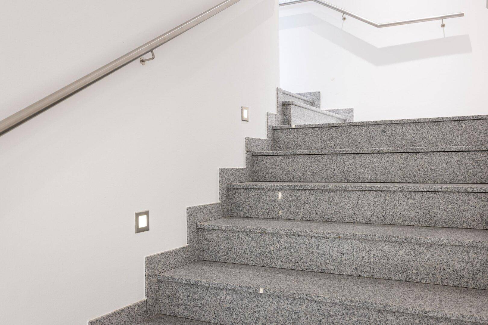 Moderner Treppenaufgang mit Granitstufen und integrierter Beleuchtung an der Wand.