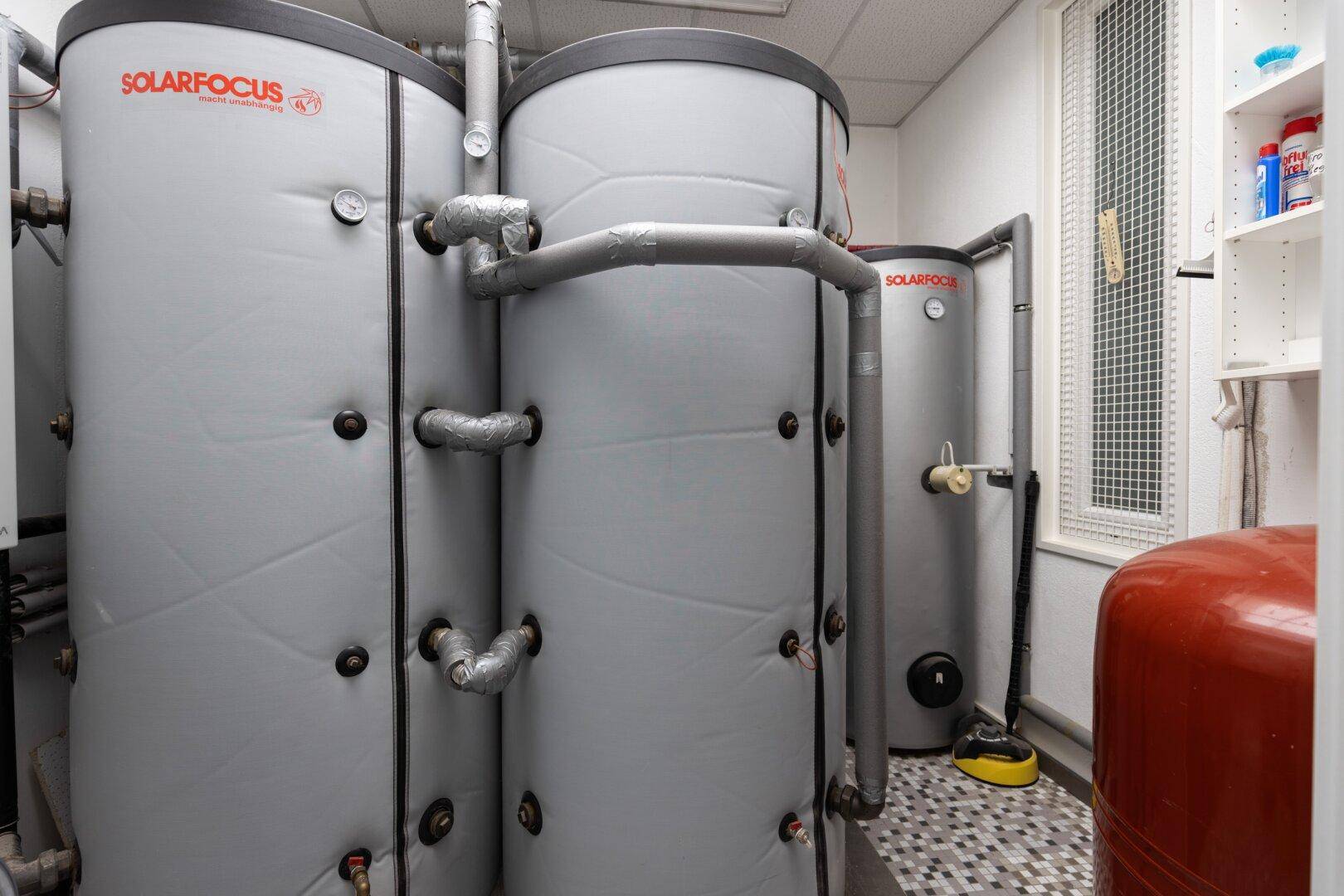 Heizungsraum mit großen Warmwasserspeichern und sichtbaren Rohrleitungen, gut isoliert.