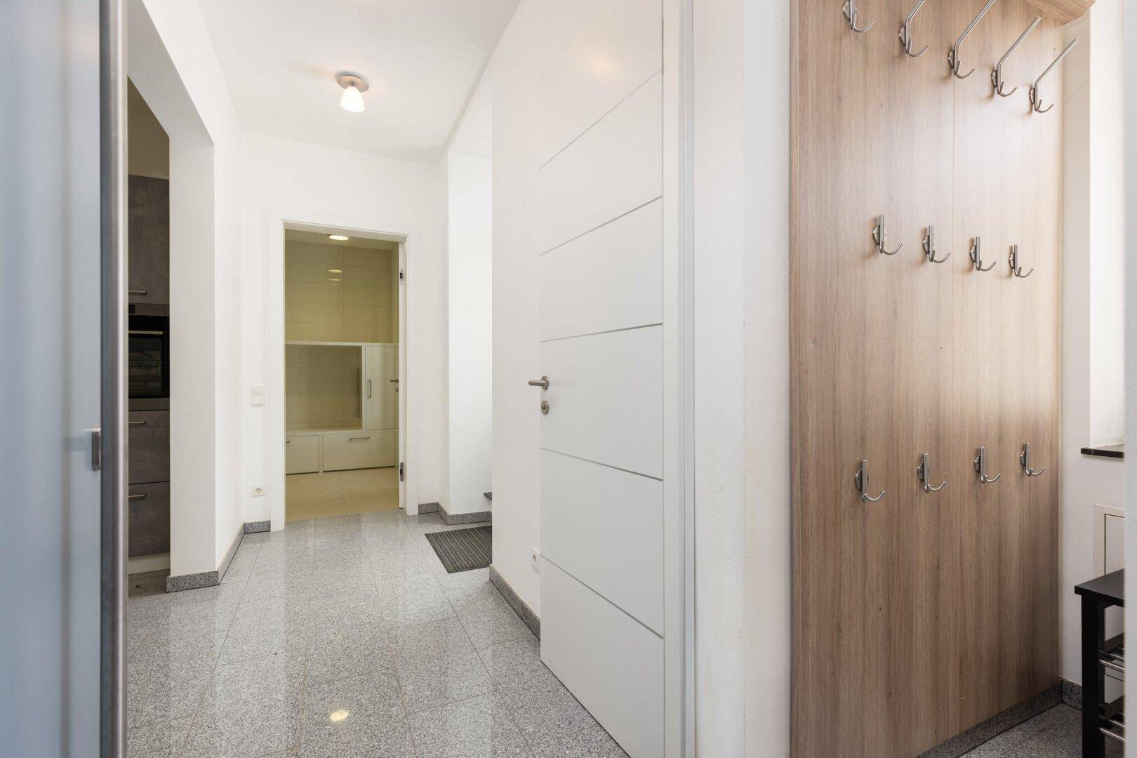 Heller Flur mit Granitboden, weißer Tür und Garderobe, führt zu weiteren Räumen.