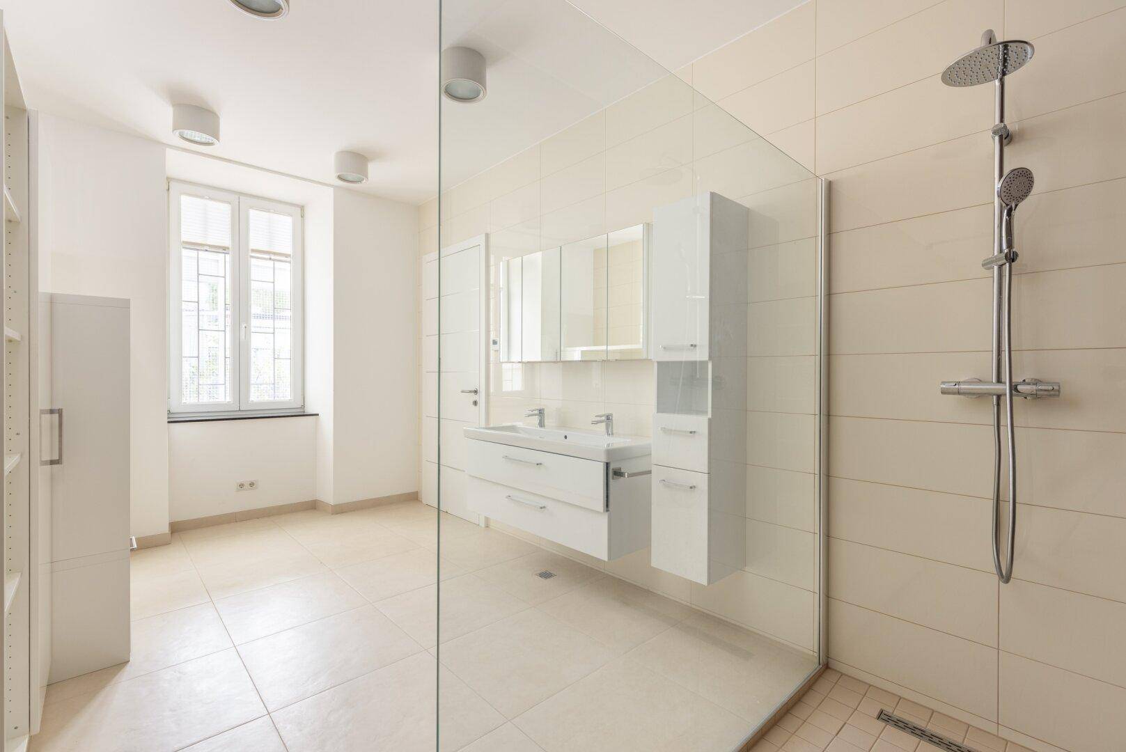 Helles Badezimmer mit Doppelwaschbecken, großer Dusche und modernen Fliesen.