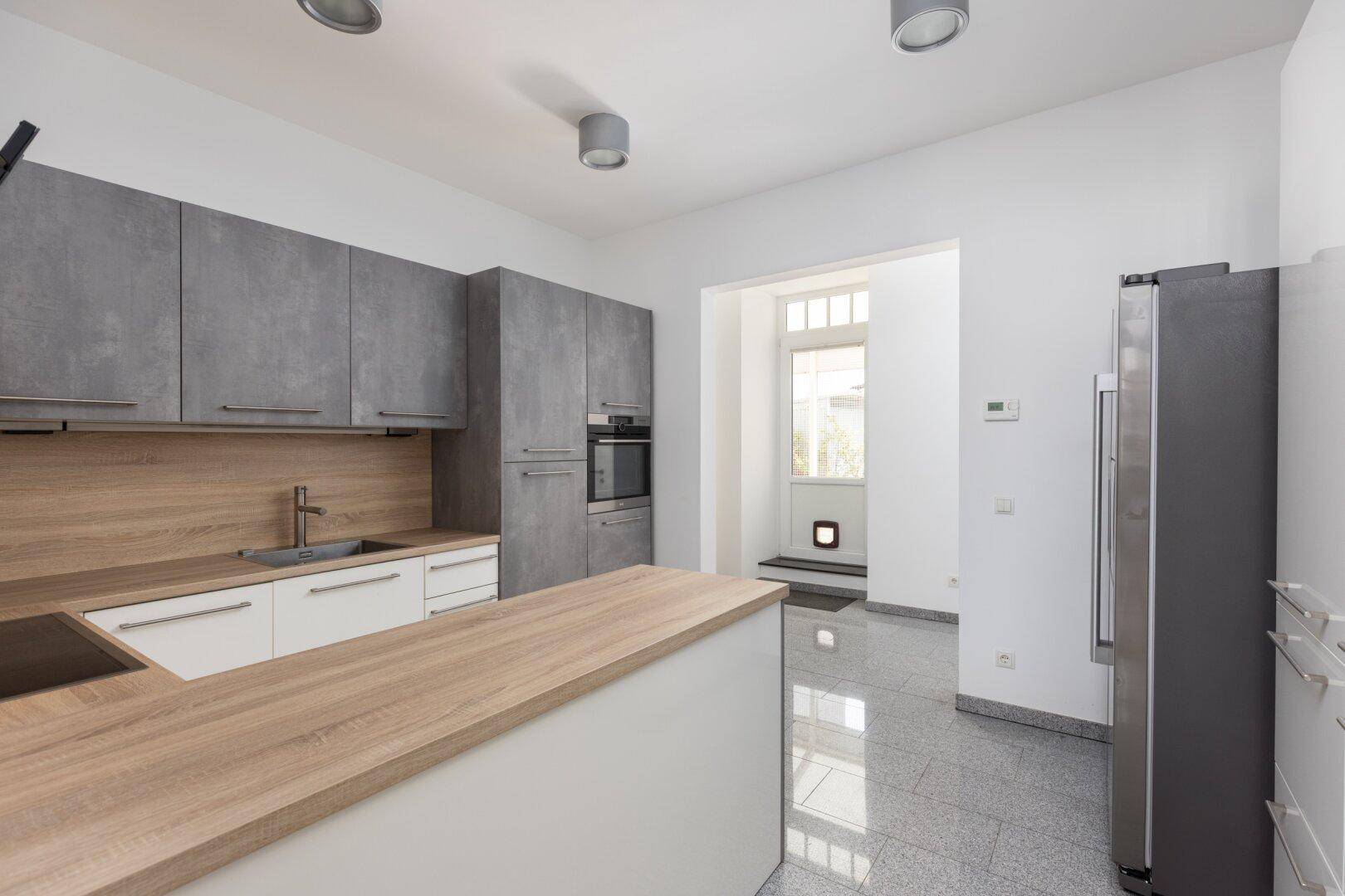 Moderne Küche mit grauen Schränken, Holzarbeitsplatte und großem Kühlschrank.