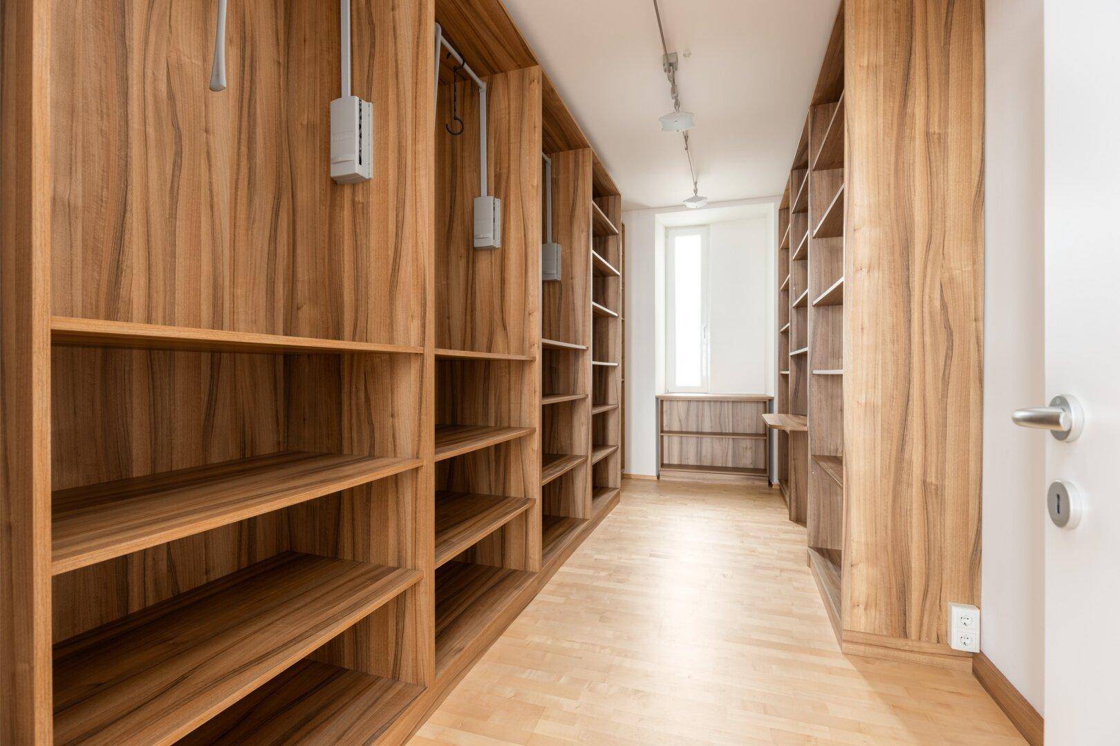 Geräumiger begehbarer Kleiderschrank mit Holzregalen und viel Stauraum.