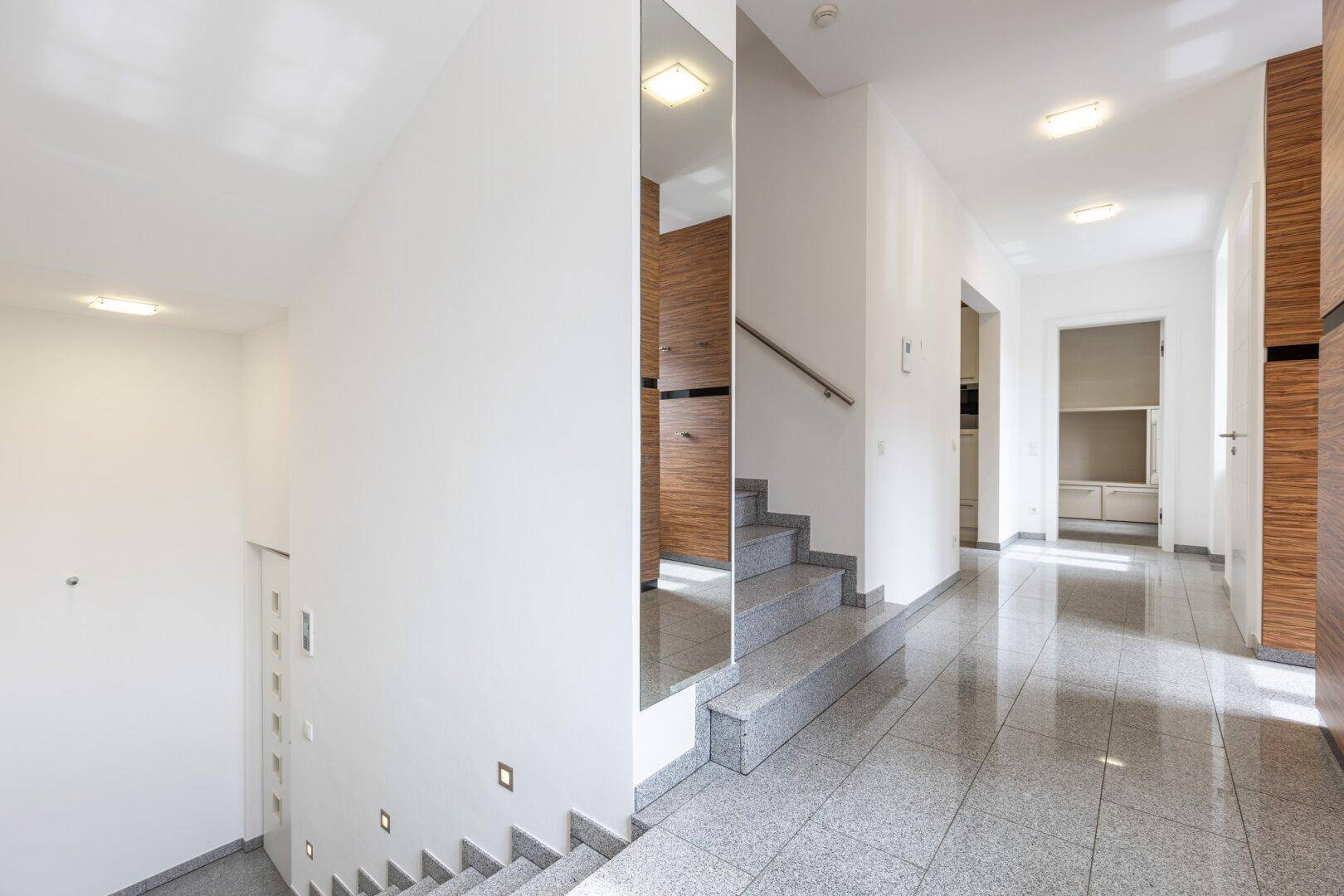 Heller Flur mit Granitboden, Treppe und modernen Spiegelelementen.