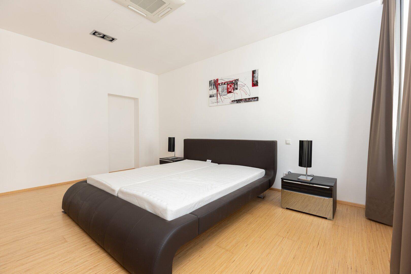 Schlafzimmer mit modernem Doppelbett, Parkettboden und weiß gestrichenen Wänden.