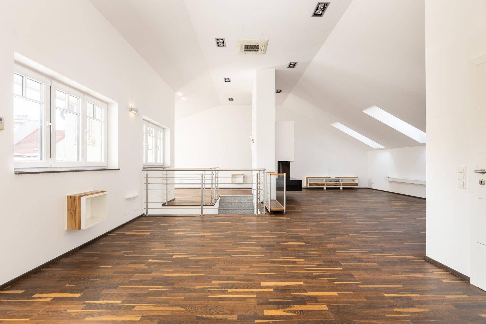 Weitläufiger offener Wohnbereich im Dachgeschoss mit Holzboden und Dachfenstern.