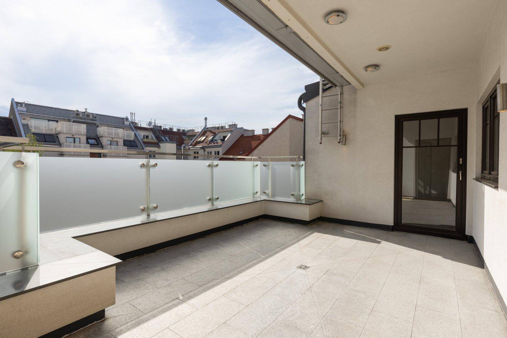 Geräumiger Balkon mit Glasgeländer und Blick auf die umliegenden Gebäude.